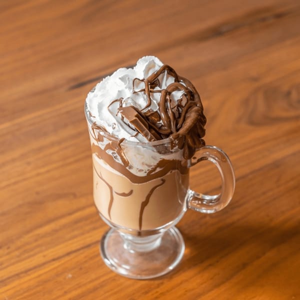 Venezuelan coffee drink with whipped cream, chocolate syrup, and chocolate bar pieces on a wooden table.