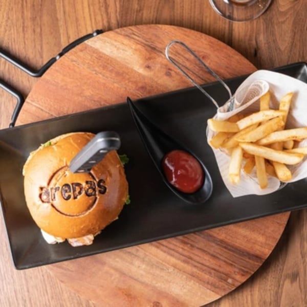 Arepas Latin Cuisine burger with "arepas" branded bun, fries, and ketchup on a black plate.