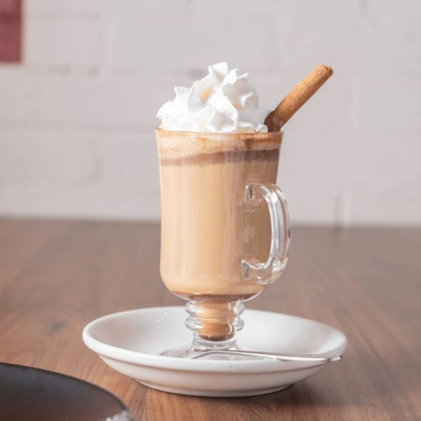 Venezuelan coffee with whipped cream and a cinnamon stick, served in a clear mug on a white saucer.