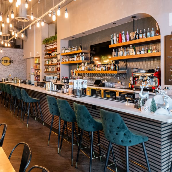 A long, well-lit bar with teal velvet stools, shelves of liquor, and holiday decorations.