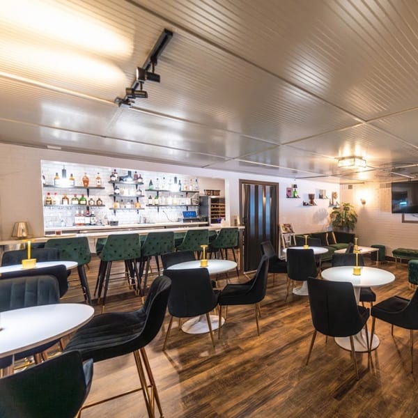 Arepas Latin Cuisine's bar area with dark green bar stools, small white tables, and a lounge area.