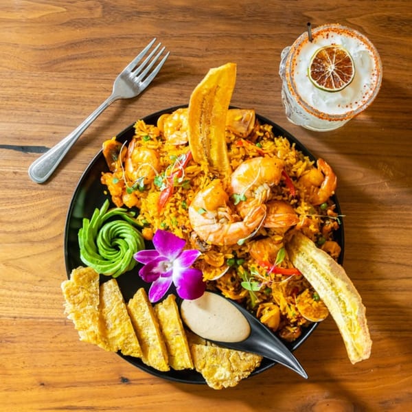 Venezuelan seafood rice with shrimp, plantains, avocado, and a cocktail on a wooden table.