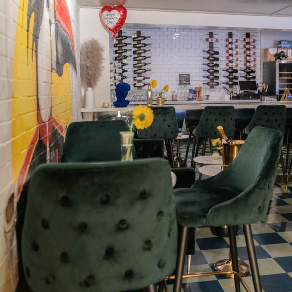 Interior of Arepas Latin Cuisine, featuring green velvet bar stools, a wine rack, and a colorful mural.