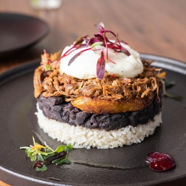 Venezuelan dish with layers of white rice, black beans, shredded beef, plantain, and a poached egg.