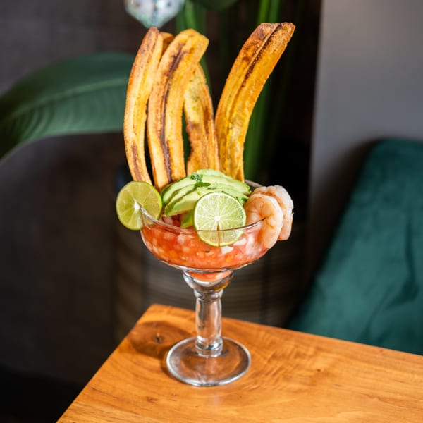 Venezuelan shrimp ceviche in a glass, garnished with avocado, lime, and plantain chips.
