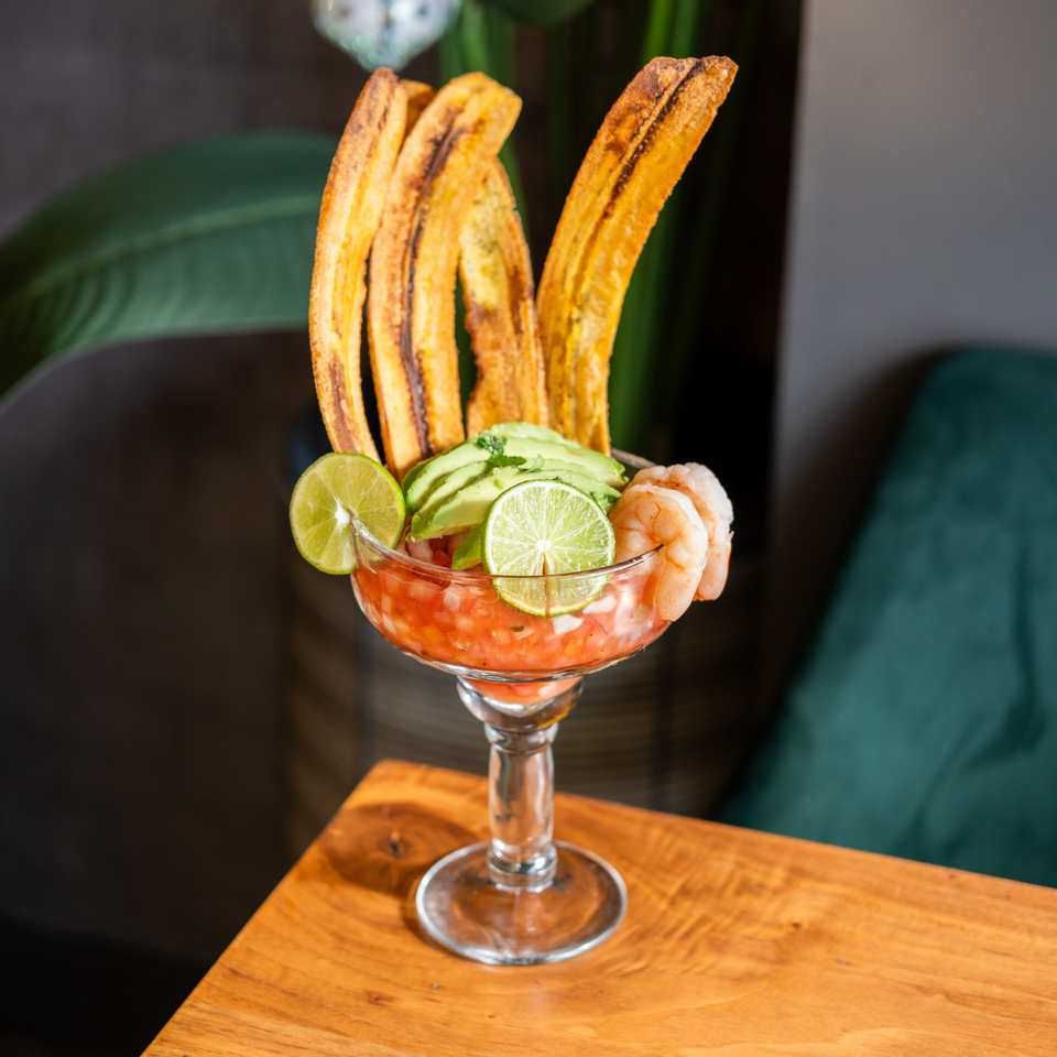 Venezuelan shrimp ceviche in a glass, garnished with avocado, lime, and plantain chips.