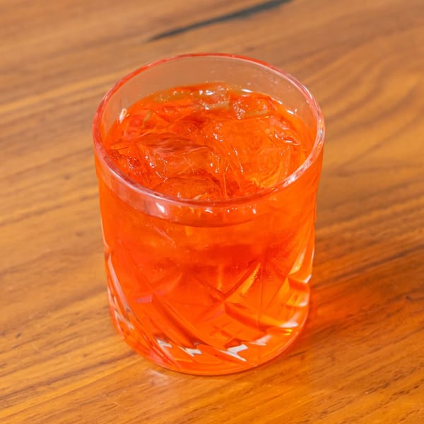 A vibrant orange cocktail with ice in a cut glass, sitting on a warm wooden table.