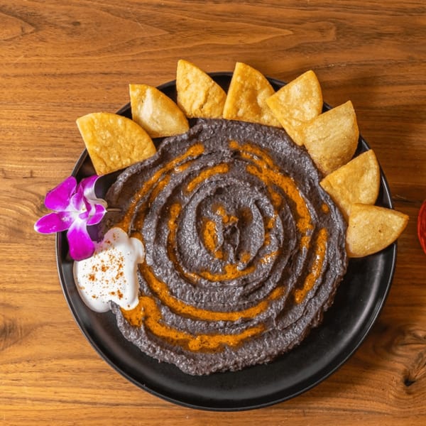 Venezuelan black bean dip with a spiral of orange sauce, white cream, and fried plantain chips.