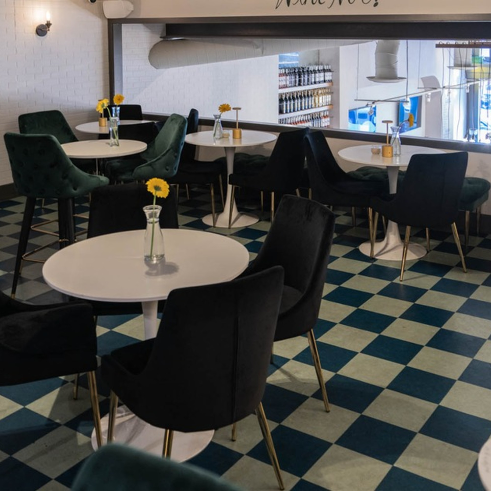 Interior of Arepas Latin Cuisine, featuring round white tables, dark velvet chairs, and a checkered floor.