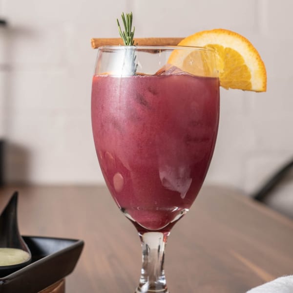 A glass of red sangria with an orange slice, cinnamon stick, and rosemary sprig.