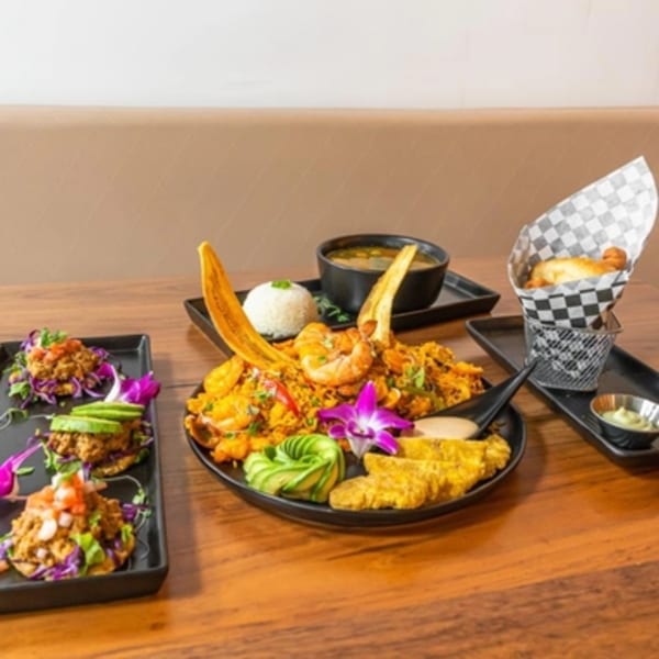 Venezuelan seafood platter with rice, shrimp, plantains, soup, and mini arepas on a wooden table.