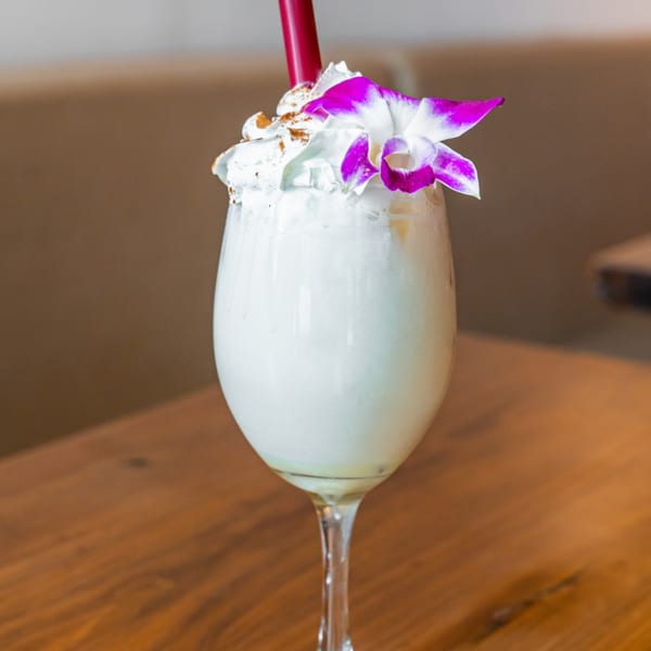 Venezuelan drink in a wine glass, topped with whipped cream, cinnamon, and a purple orchid.