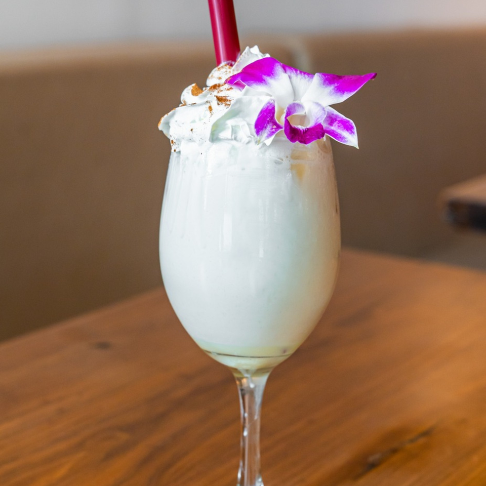Venezuelan drink in a wine glass, topped with whipped cream, cinnamon, and a purple orchid.