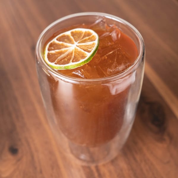 Iced tea with a dried lime slice on top, served in a double-walled glass on a wooden table.