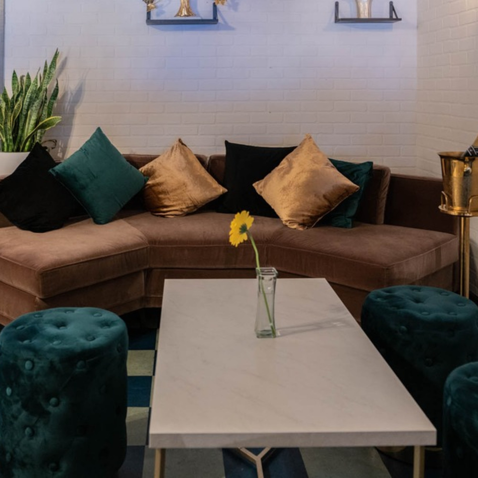 A cozy lounge area with a brown sectional sofa, teal and gold pillows, and a white coffee table.