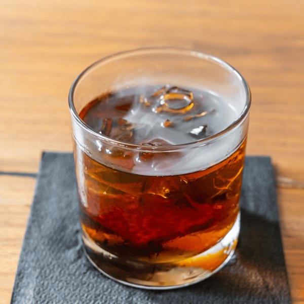 A glass of dark iced tea or cocktail on a black coaster, on a wooden table.