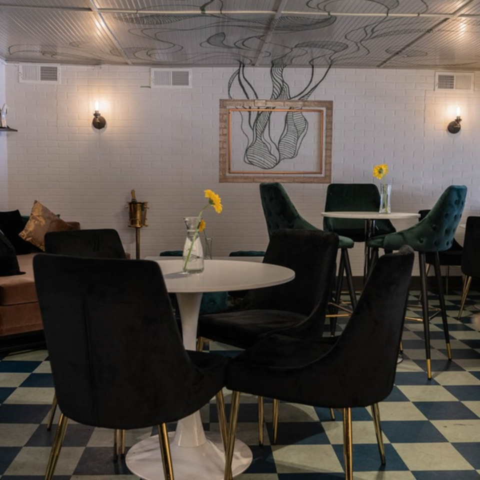 Interior of Arepas Latin Cuisine, featuring black and teal chairs, white tables, and a checkered floor.
